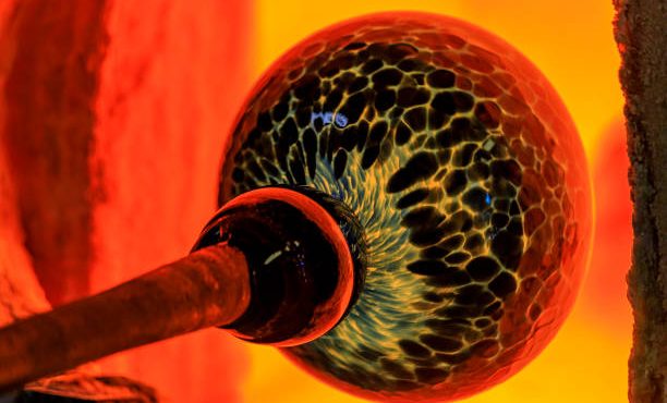 glass in furnace Glass blower manufacturing process - working on a bubble of melted glass on a rod by heating it up by hand in a kiln at a glass maker's workshop